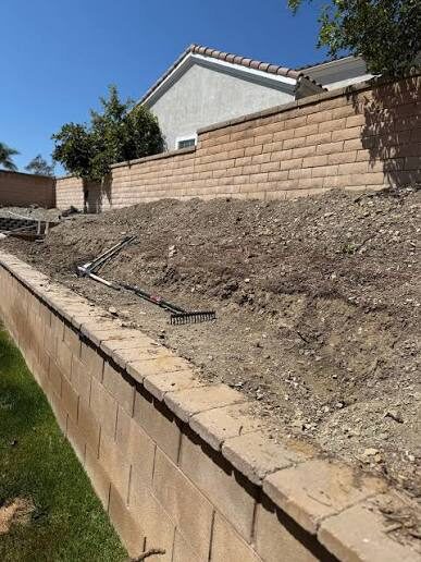 Mid-job retaining wall with backfill graded in behind the block and a rake resting on the slope